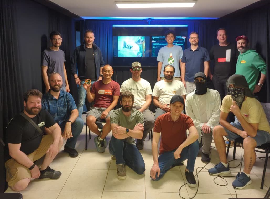 Group photo of the summit attendees at Casa 21 in São Paulo, roughly seventeen developers posed in front of a presentation screen. Several have their faces covered for privacy.