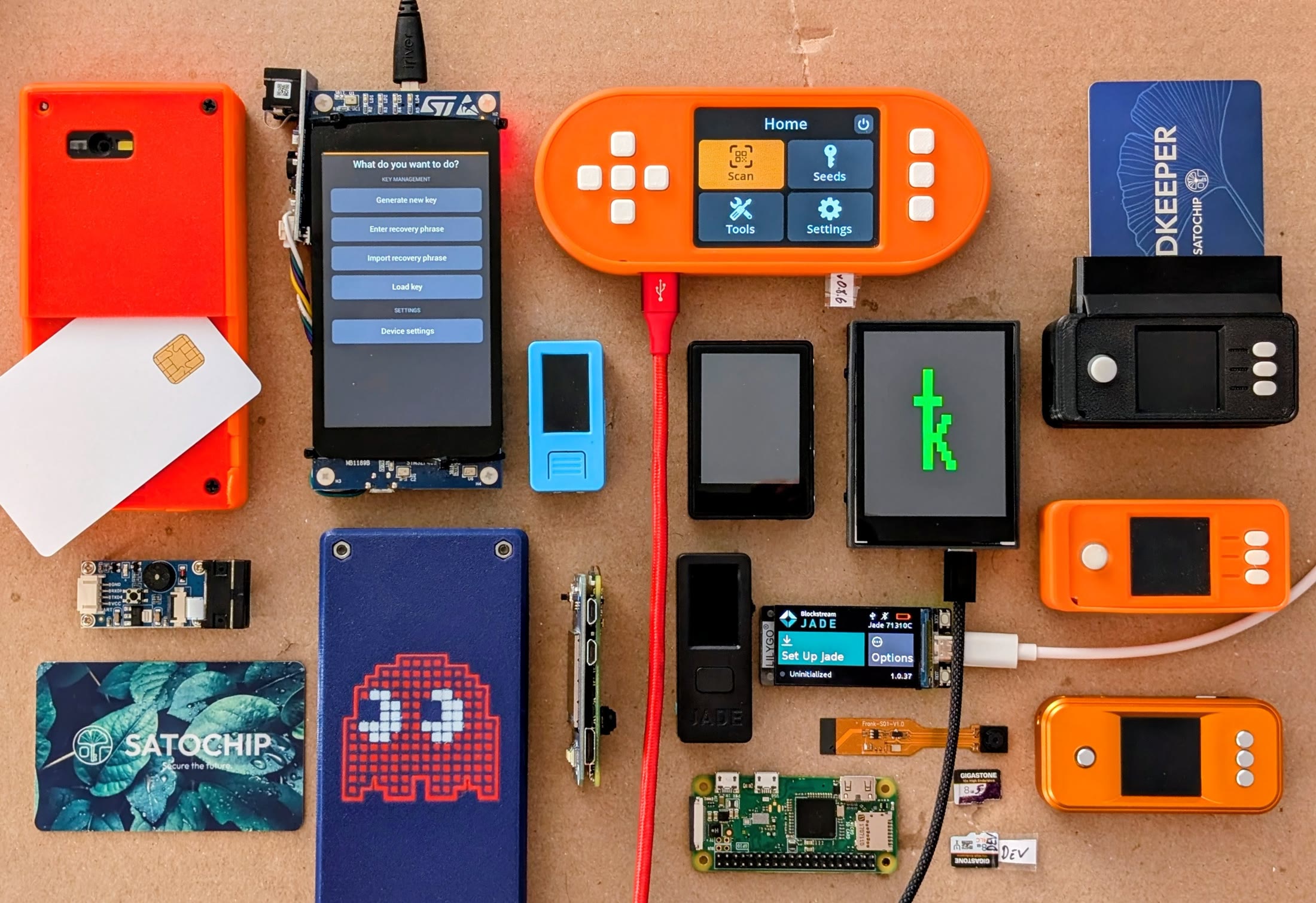 A tabletop covered with more than a dozen DIY bitcoin signing devices in various enclosures, alongside loose components and smartcards.