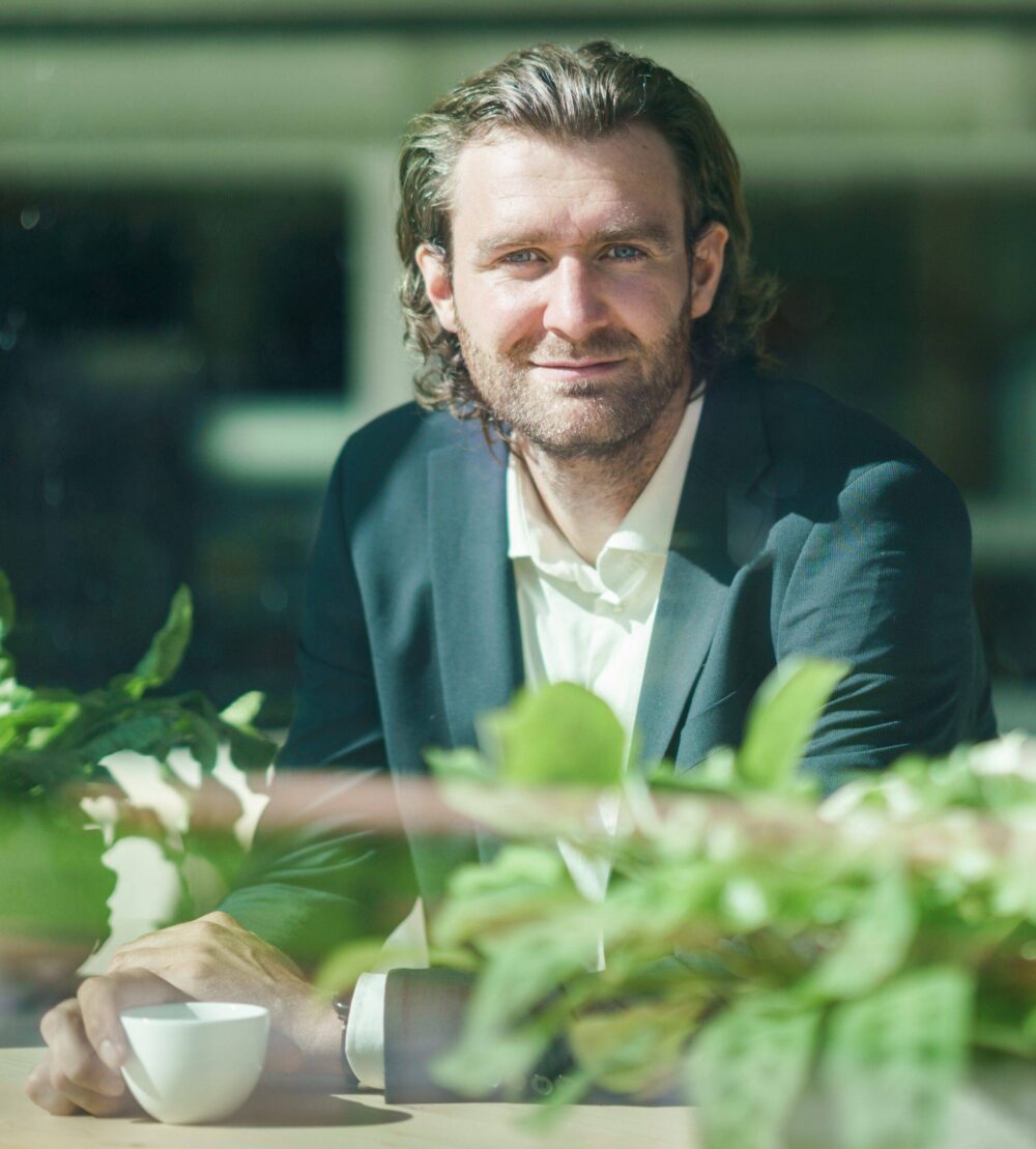 Rob Segers Bitcoin advisor in suit behind window with cup of coffee
